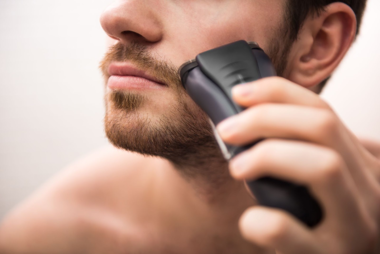 Photo of a man using an electric shaver to trim his beard