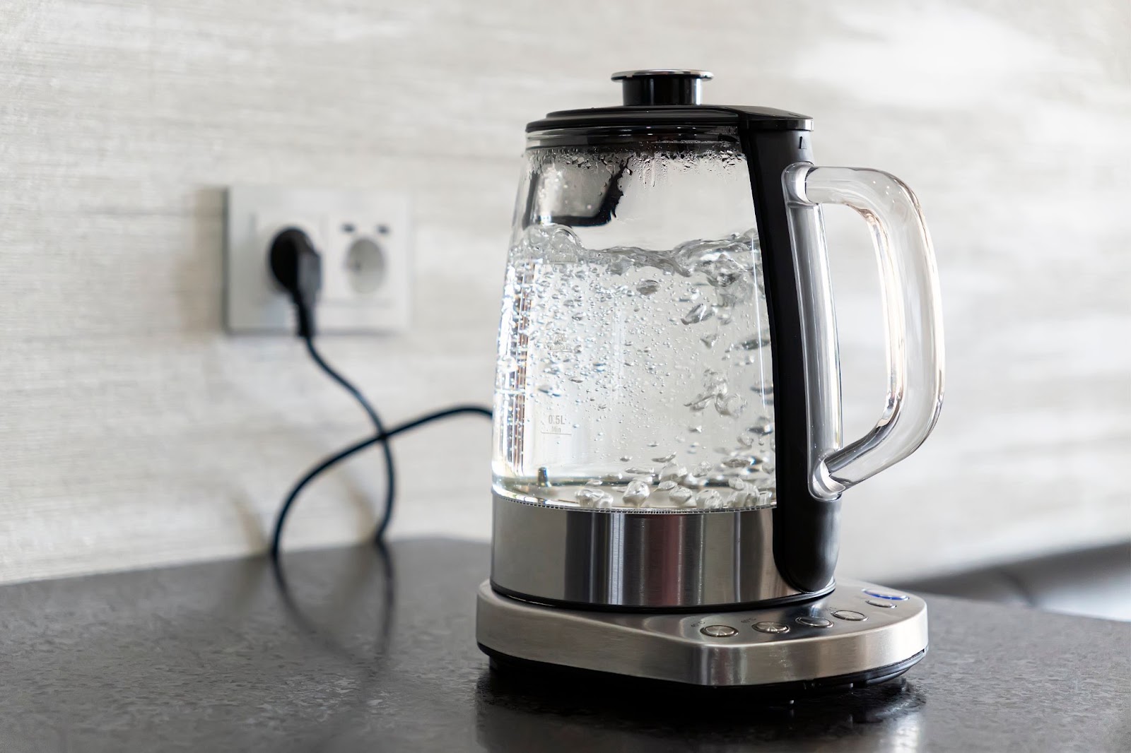 Glass electric kettle boiling water on its base, plugged into a wall outlet