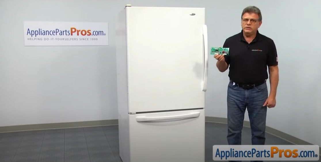 Technician holding a temperature control board next to a white bottom-freezer refrigerator