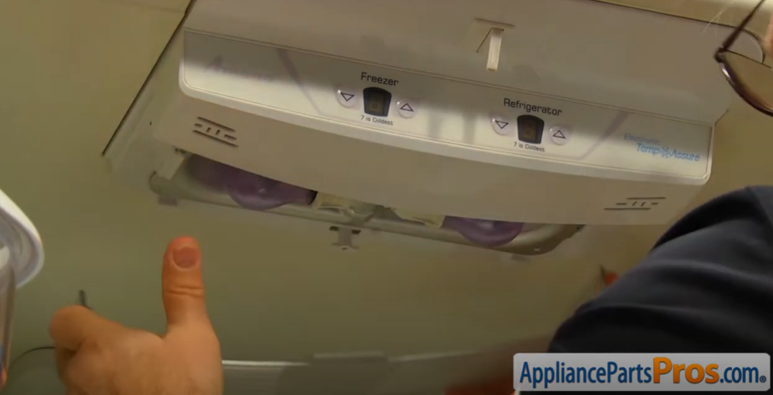Freezer and refrigerator temperature control housing on a fridge ceiling with a hand pointing