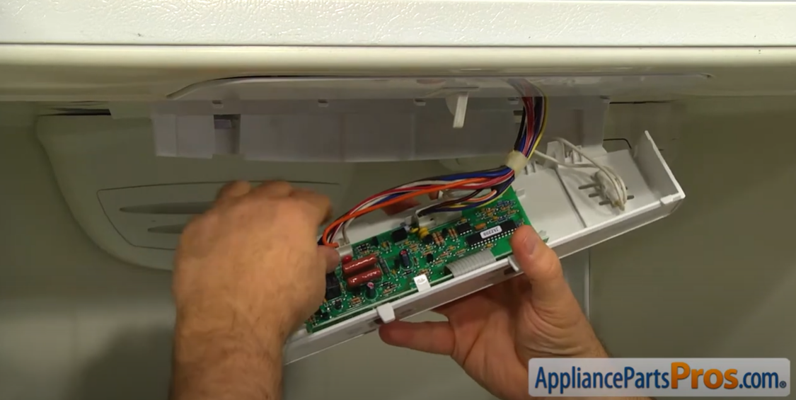 Hands disconnecting wire harnesses from a refrigerator temperature control board