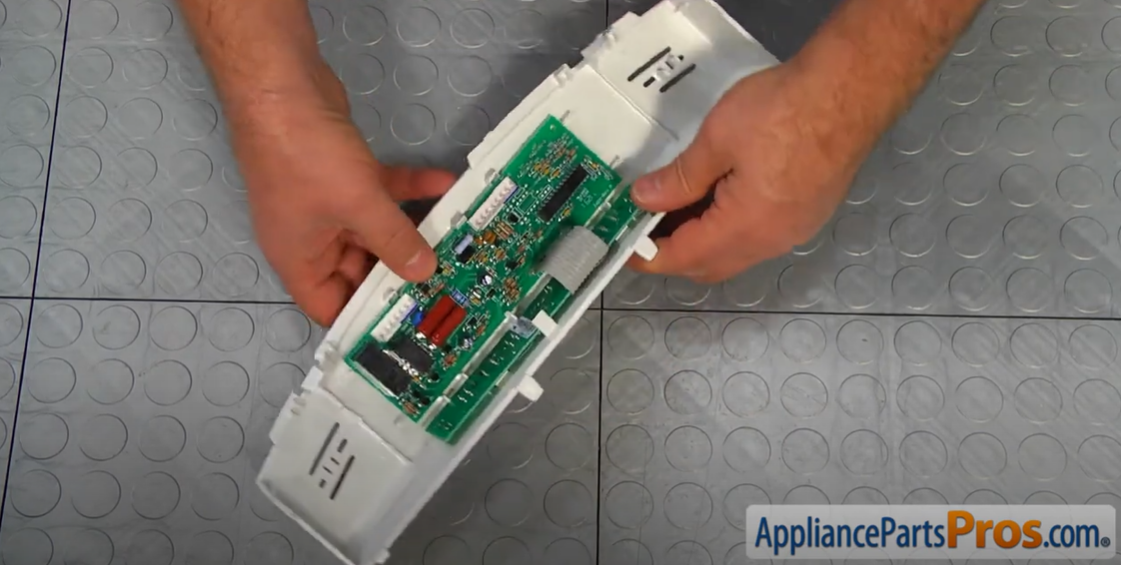 Hands holding a refrigerator temperature control board mounted in its plastic housing