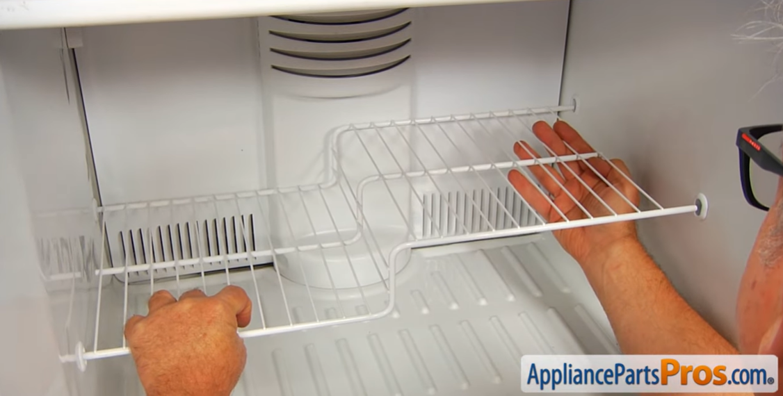 Hands sliding a white wire shelf back into a freezer compartment