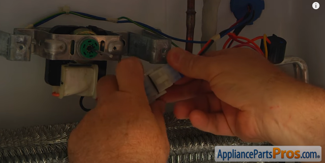 Hands disconnecting the wiring plug from the evaporator fan motor above the coils