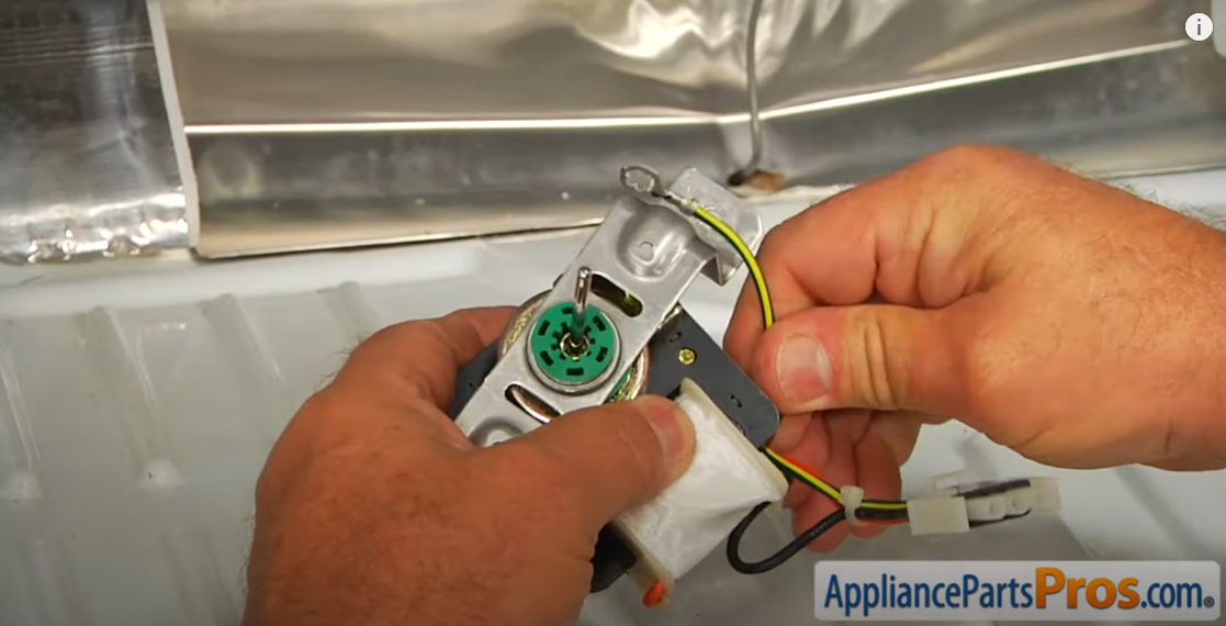 Hands holding a new evaporator fan motor on its metal bracket with wiring attached