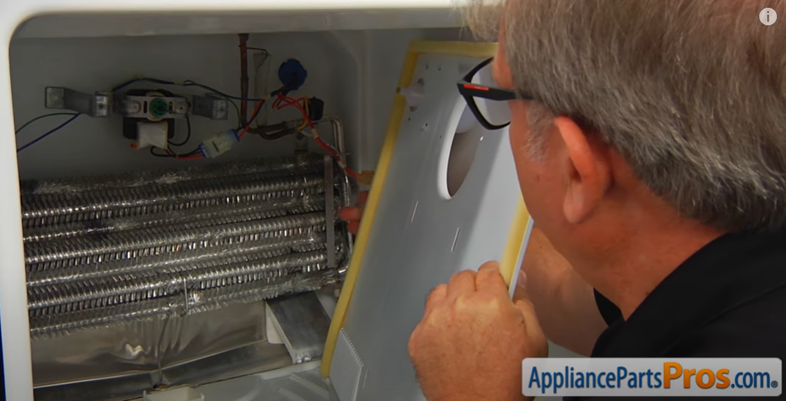 Technician fitting the metal fan cover back over the exposed evaporator coils and fan motor