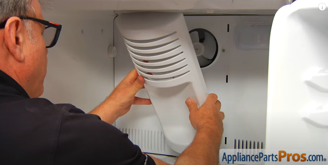 Technician fitting the vented plastic evaporator cover back onto the freezer's rear wall