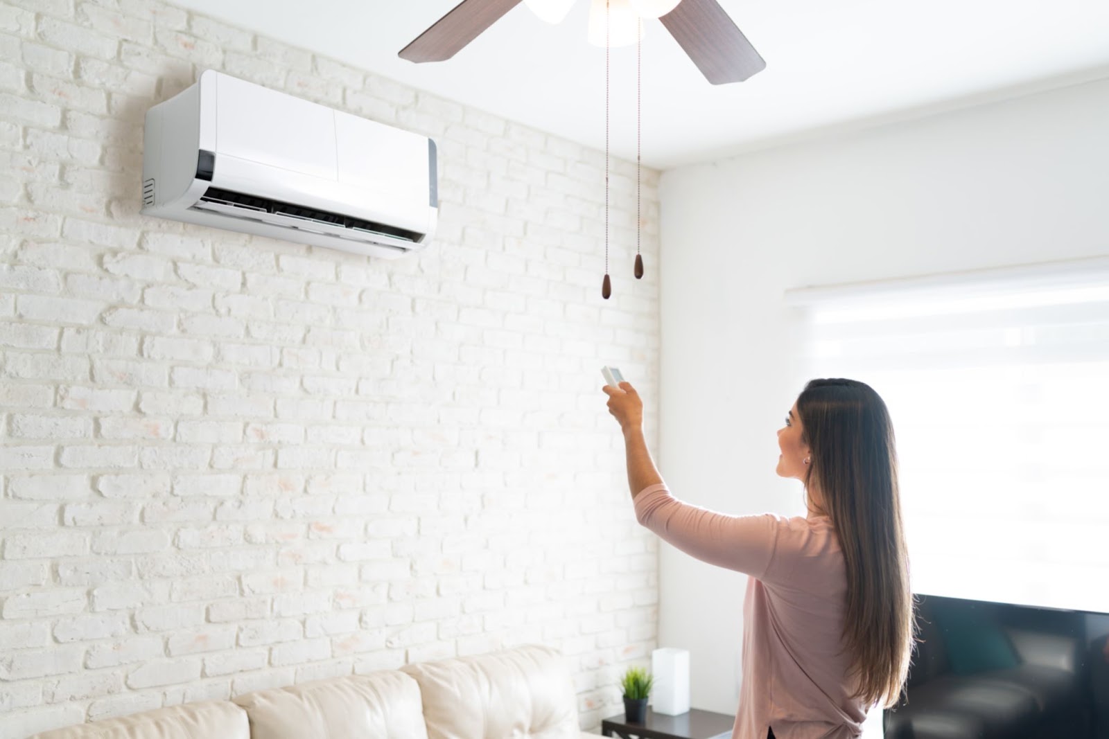 Woman using a remote to run a ductless mini-split air conditioner mounted high on a brick wall