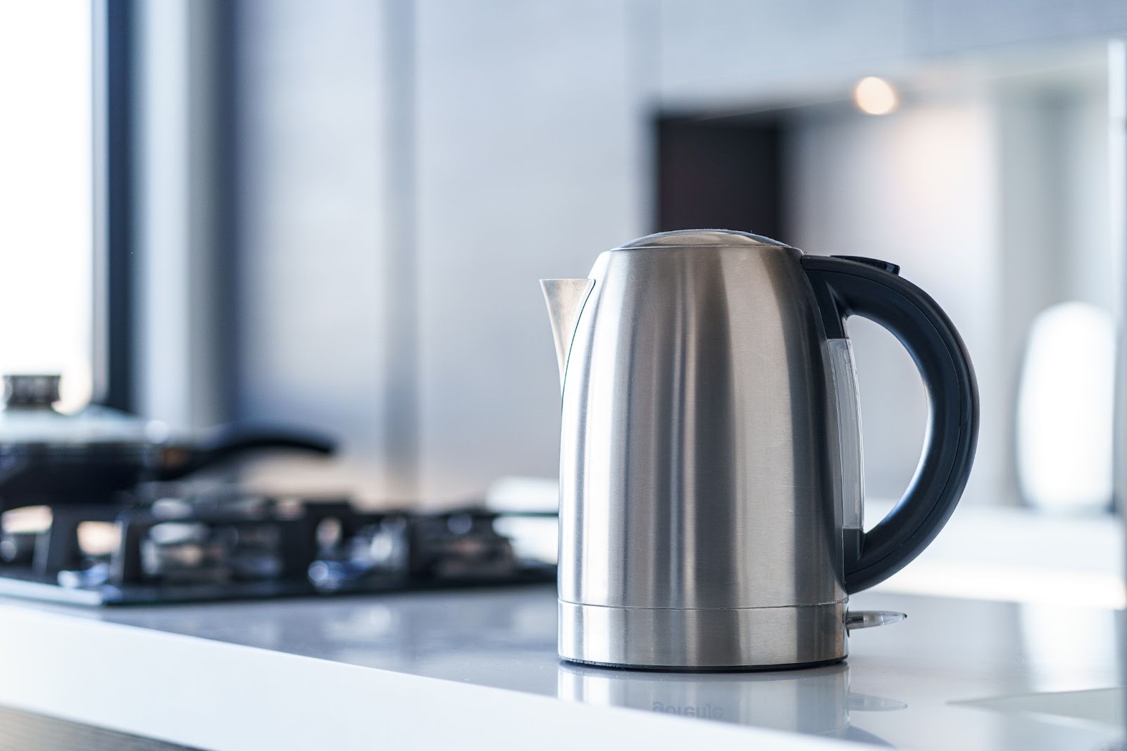 Stainless steel electric kettle on a white counter near a gas stovetop