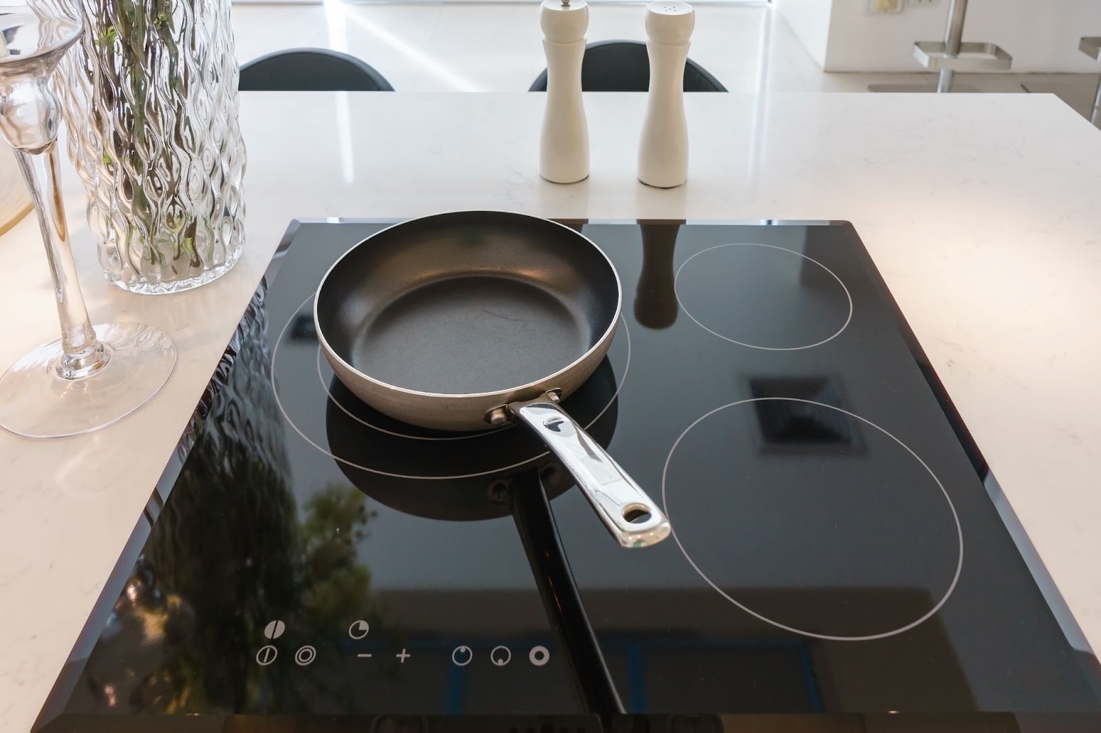 Frying pan on a black glass cooktop with four marked burner rings and touch controls