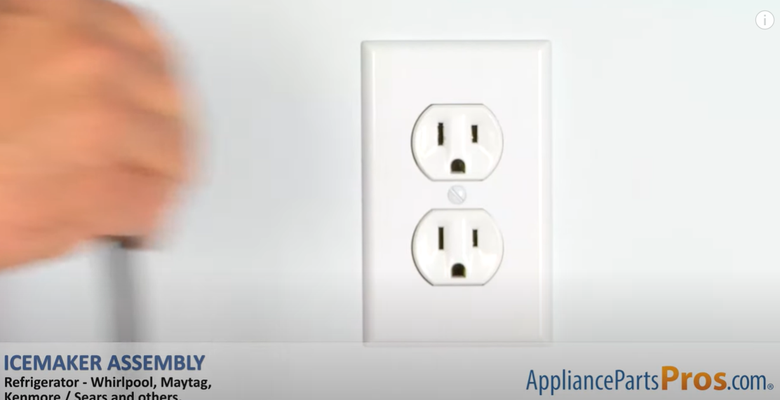 Hand reaching toward a wall outlet to unplug the refrigerator before installing an ice maker