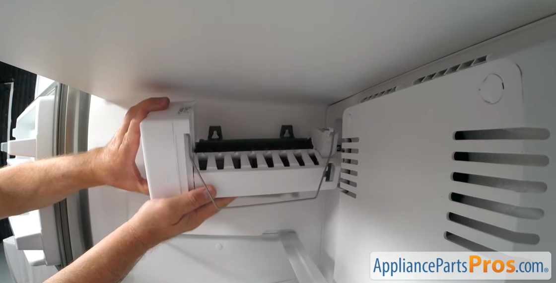 Hands lifting a new ice maker assembly into place at the top of a freezer compartment