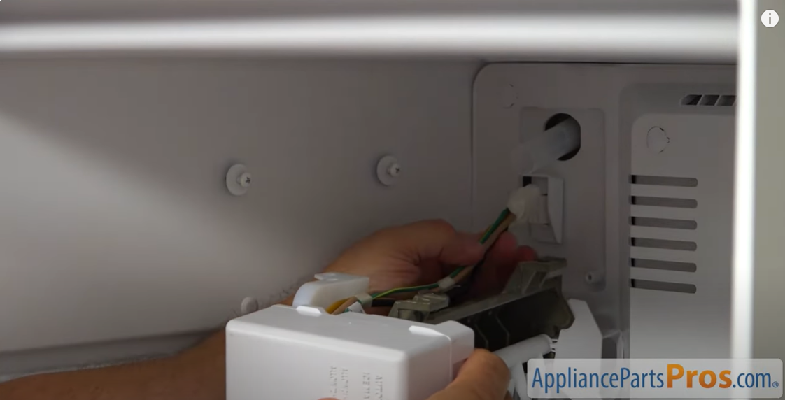 Hands connecting the ice maker wiring harness to the outlet on the back wall of a freezer compartment