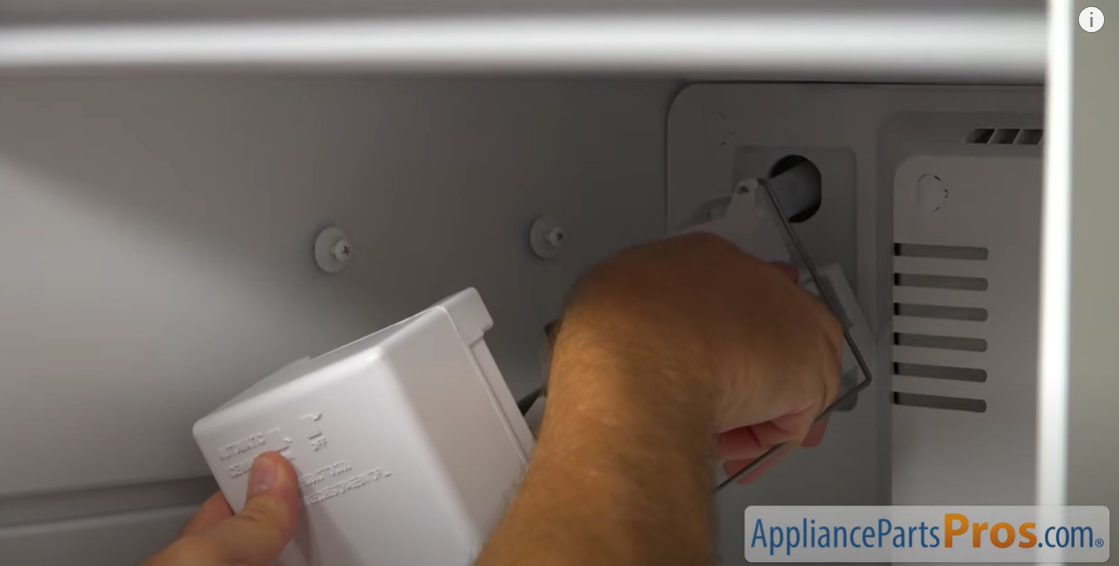Hands mounting an ice maker onto the screws on a freezer side wall