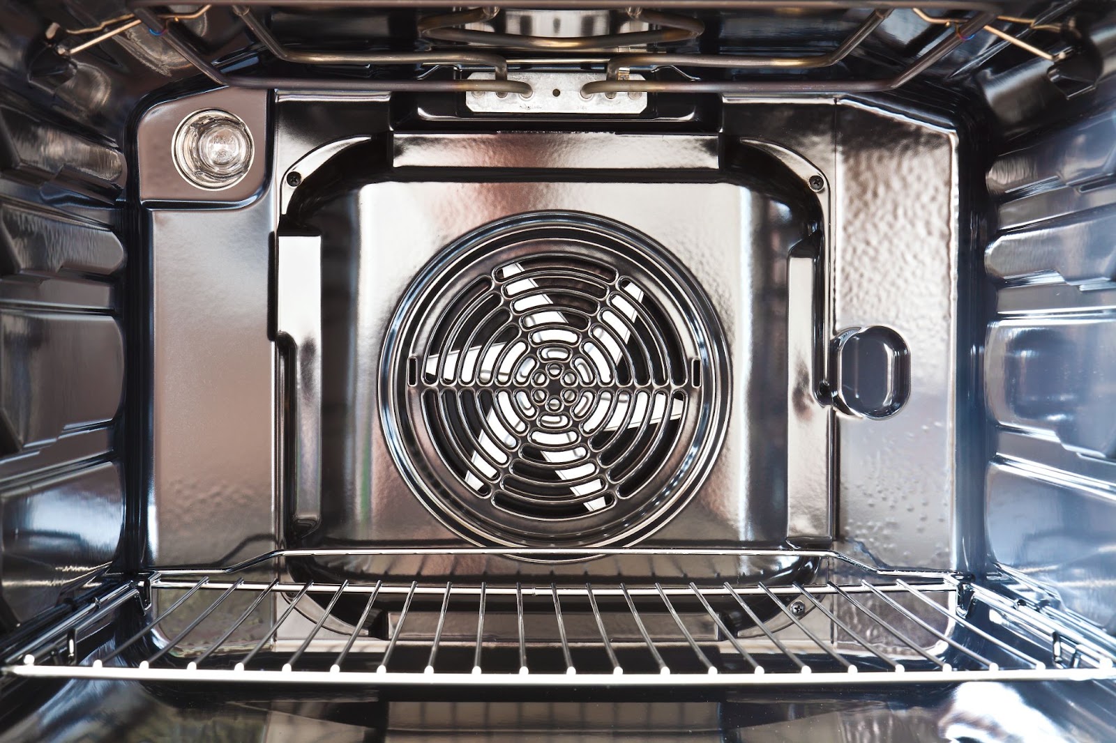 Convection fan cover on the back wall of an empty oven with a wire rack