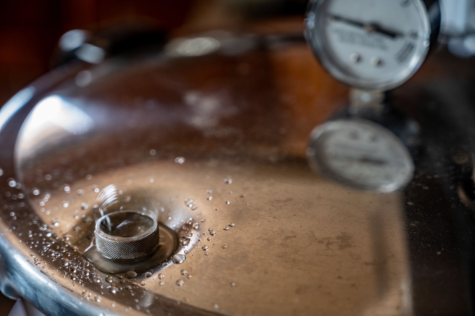 Close-up of a stainless pressure cooker lid with a vent valve and pressure gauge