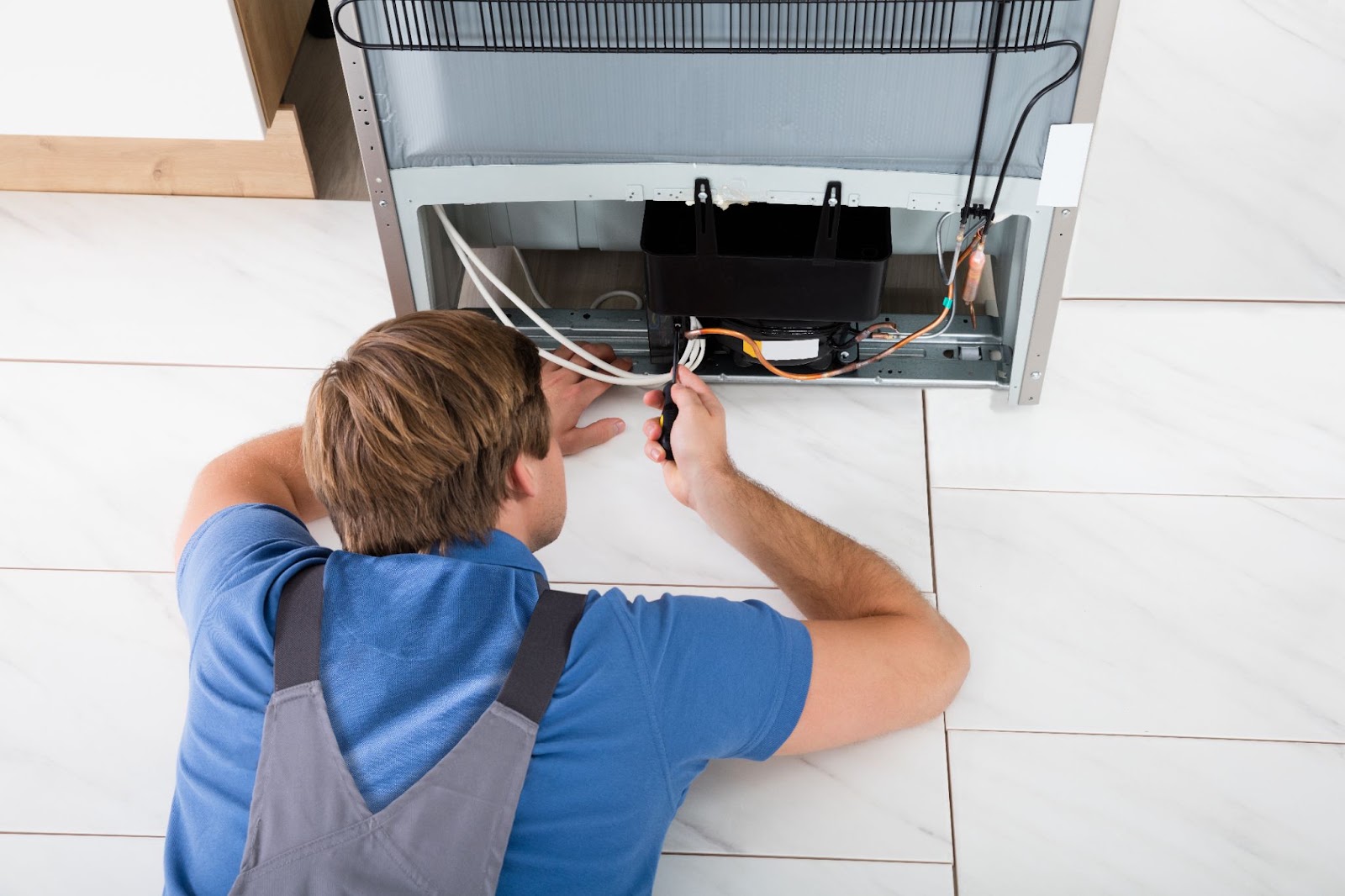 Technician lying on the floor working on wiring at the bottom of a refrigerator