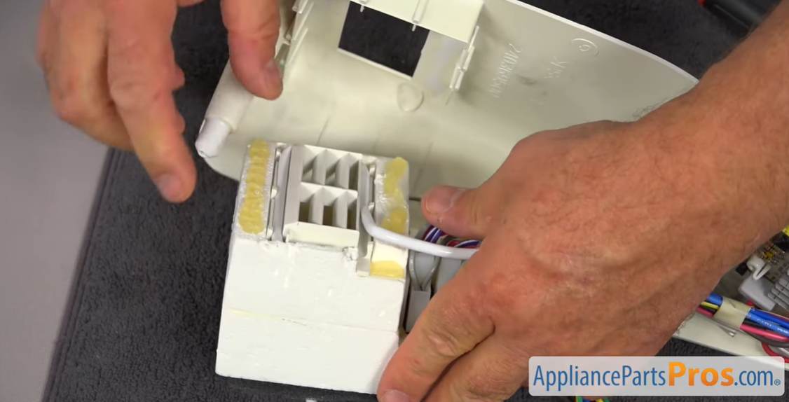 Hands sliding the thermostat sensing tube out of its insulation inside the refrigerator control housing