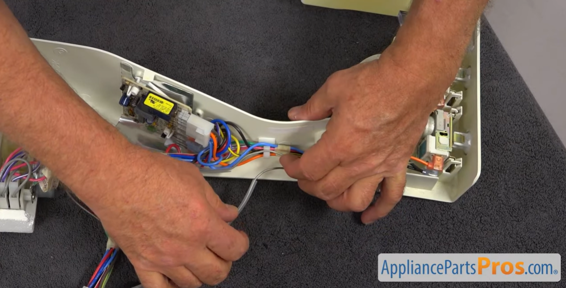 Hands removing wires from the thermostat inside an open refrigerator control housing