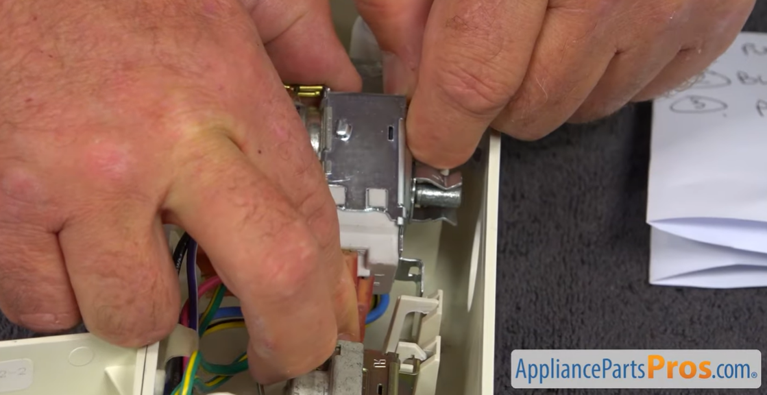 Hands pressing a new thermostat into its bracket inside the refrigerator control housing