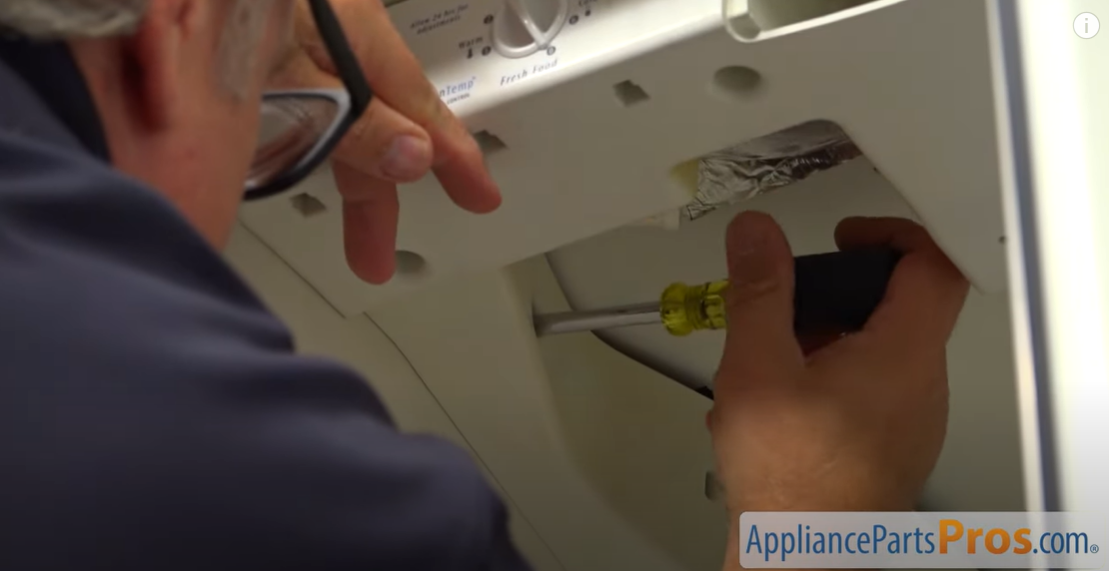 Technician using a screwdriver to secure the control housing to the refrigerator ceiling