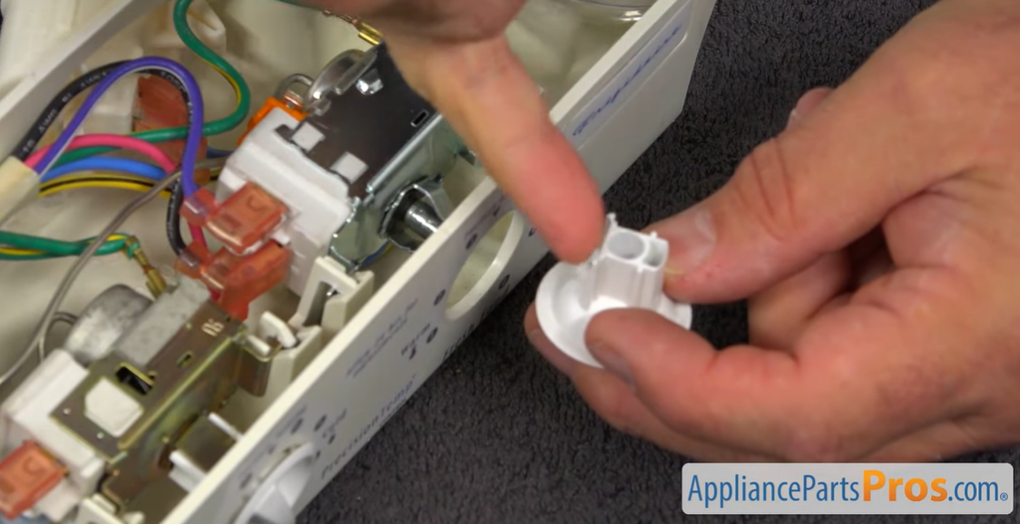 Fingers pointing to the shaft opening on a refrigerator thermostat control knob above the control housing