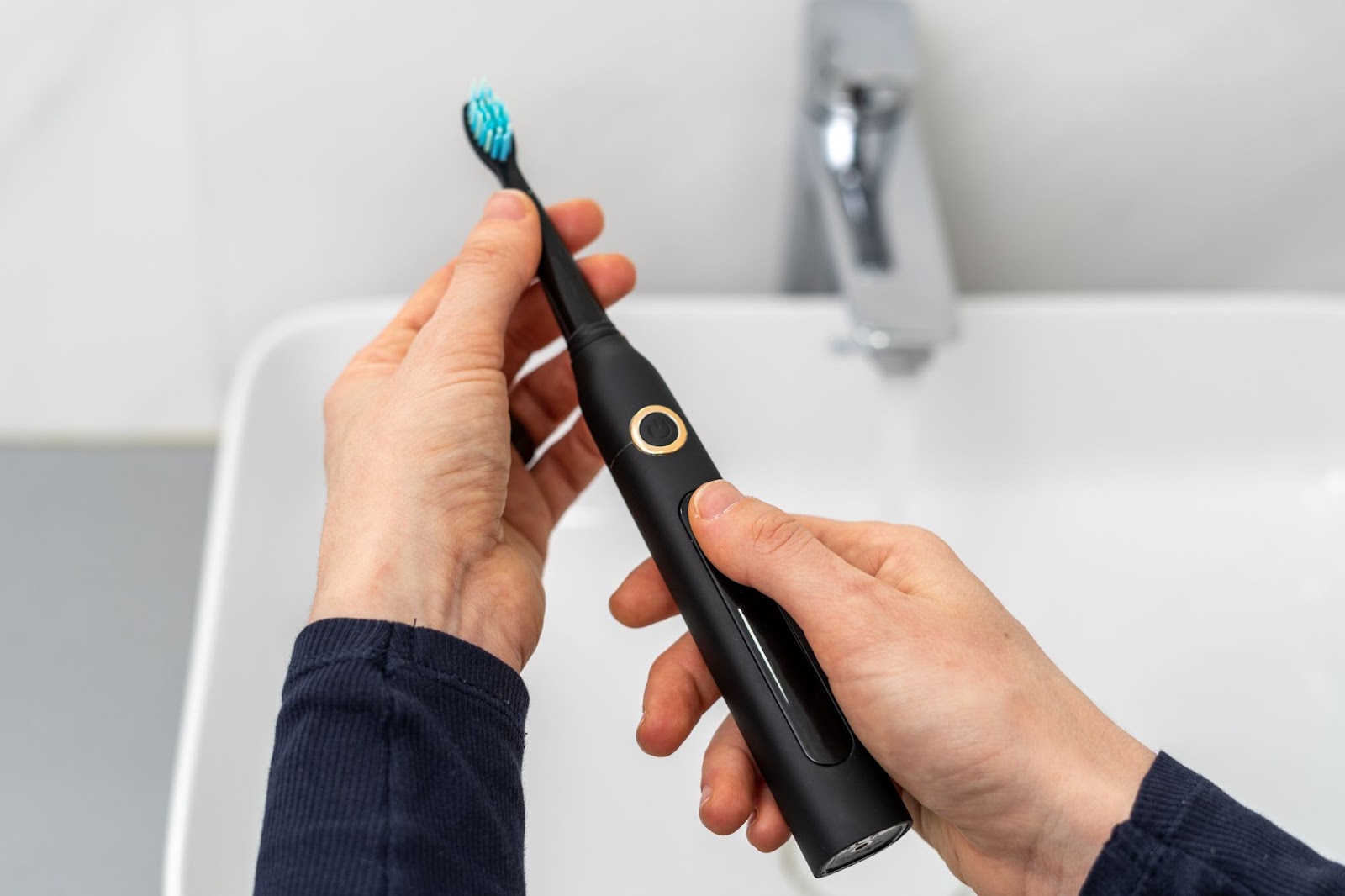Hands holding a black electric toothbrush with a blue-bristle head over a sink