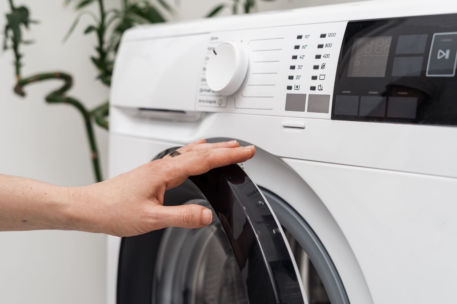 Hand opening the door of a white front-load washer with a digital control panel