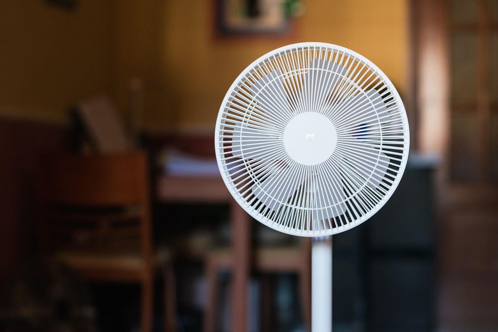 White pedestal stand fan with a round grille in a dim room