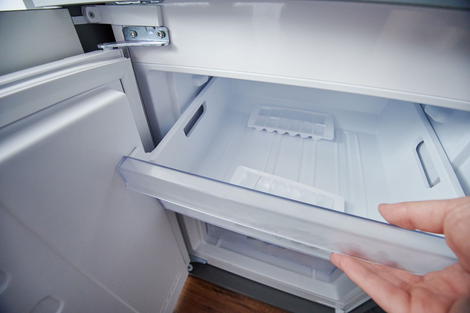Hand pulling open an empty freezer drawer with ice cube trays inside