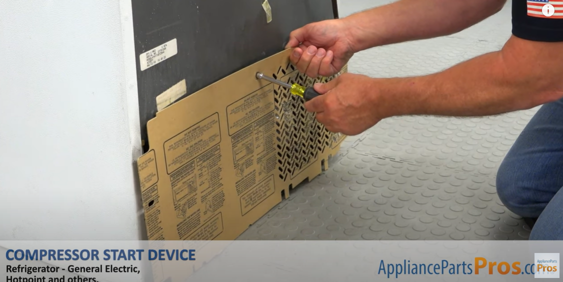 Hands using a screwdriver to fasten the rear access cover on the bottom back of a refrigerator