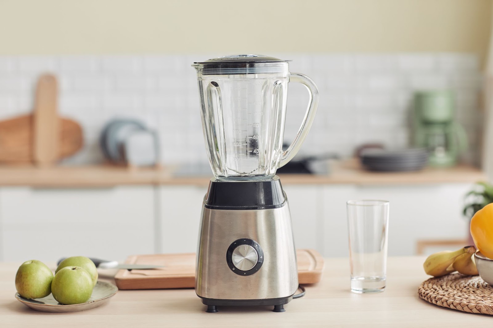 Countertop blender with a glass jar and stainless base next to apples and a drinking glass