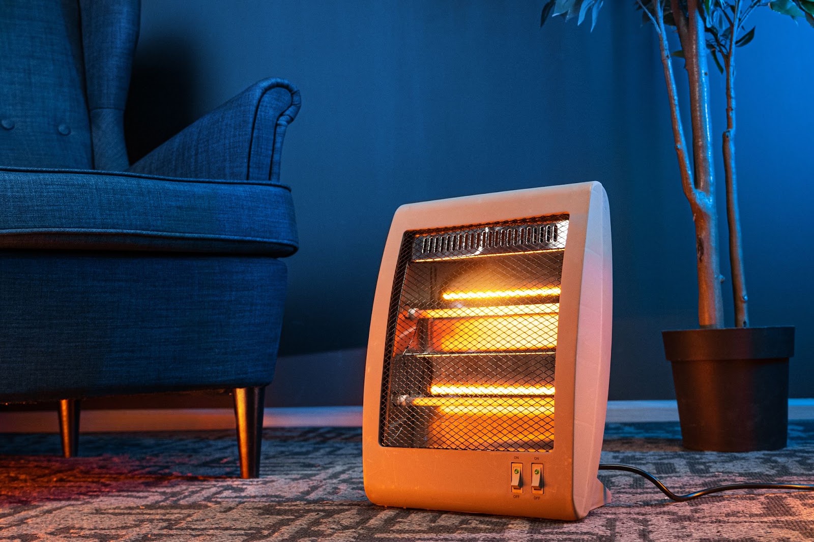 Small electric space heater with glowing elements on a rug next to an armchair